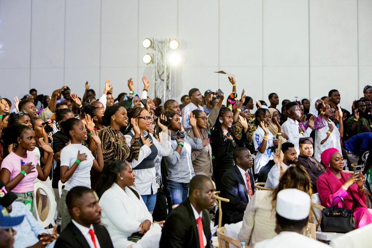 Vibrant crowd of diverse event attendees at a conference or seminar, many raising hands and engaging actively, showcasing dynamic participation and inclusive atmosphere in a professional setting.