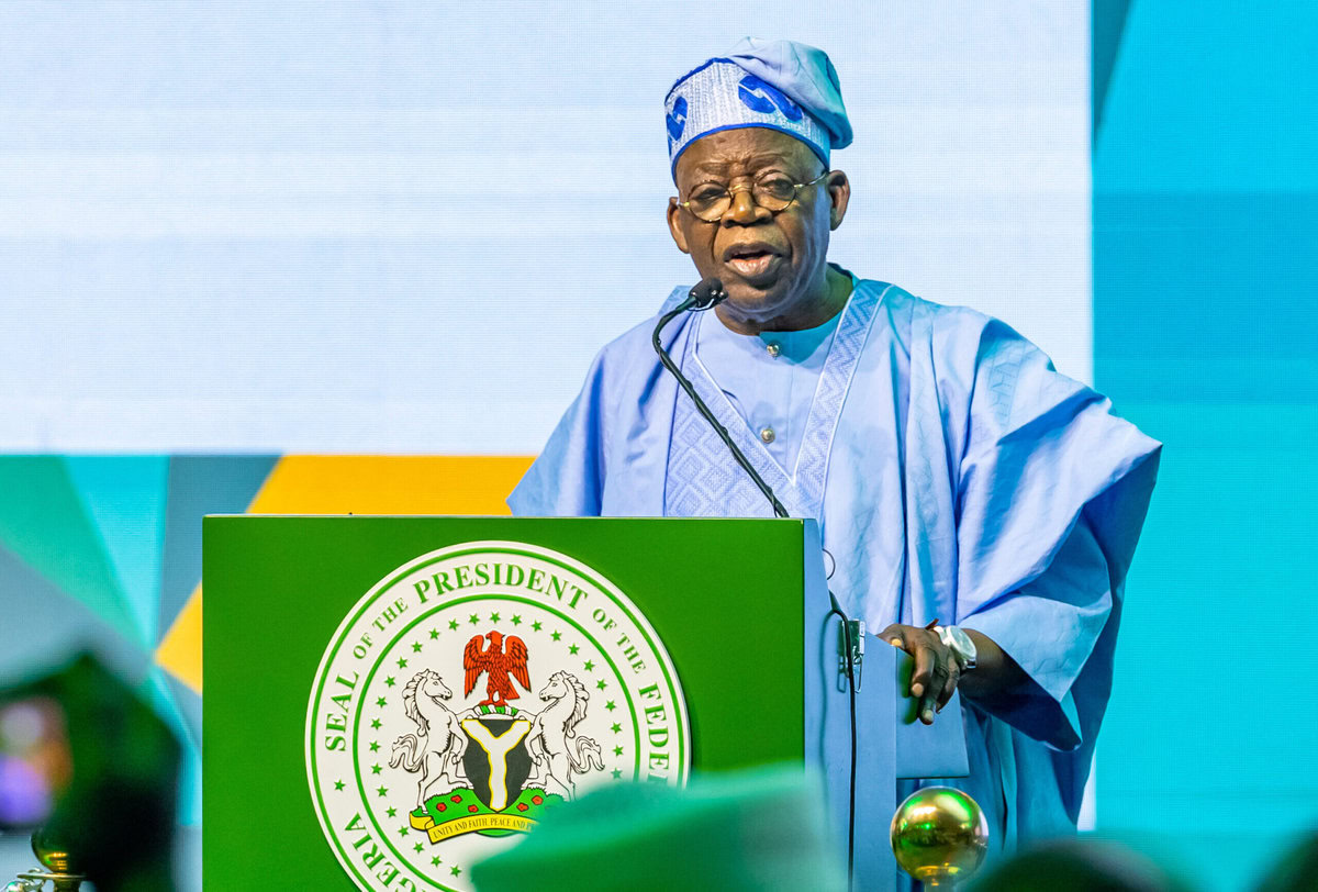 Senior Nigerian politician delivering speech at official event wearing traditional attire and standing behind a podium with the presidential seal.